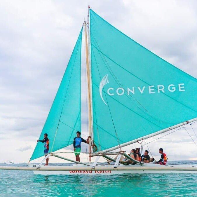 A boat with a teal sail on which the Converge logo is printed